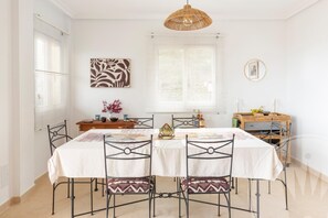 A dining area with a table set for four, surrounded by chairs, a hanging light fixture, and a decorative wall piece. - La Manga Club Monte Verde Apartment 618 (Cartagena)