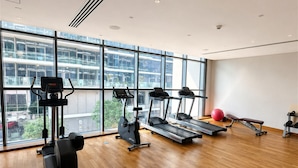 A gym with treadmills, elliptical machines, and a red exercise ball, with large windows and wooden flooring. - Pure Voyage Damac Hills (Dubai)