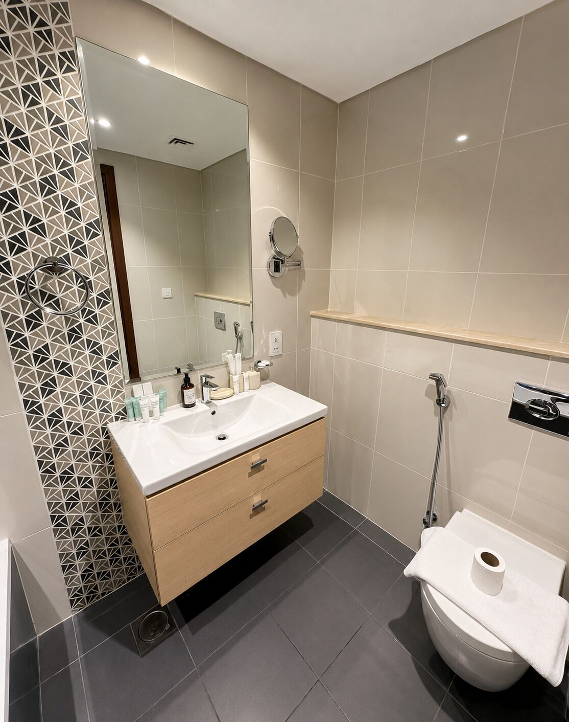 A modern bathroom with a white sink, wooden cabinet, and a toilet.