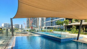 A modern outdoor swimming pool with a clear blue water surface, surrounded by a glass railing and a shaded area. - Pure Voyage Damac Hills (Dubai)