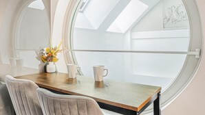 A room with a round window, a wooden table, two chairs, and a vase with flowers. - Market Square Luxury | Modern 2-Bed City Retreat (Nottingham)