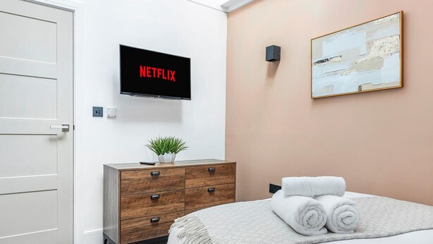 A hotel room with a bed, a dresser, a wall-mounted TV displaying 'NETFLIX,' a painting, and a door. - Market Square Luxury | Modern 2-Bed City Retreat (Nottingham)