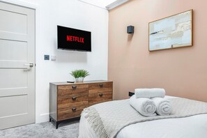 A hotel room with a bed, a dresser, a wall-mounted TV displaying 'NETFLIX,' a painting, and a door. - Market Square Luxury | Modern 2-Bed City Retreat (Nottingham)