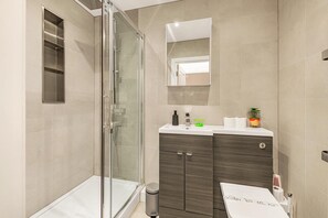 Un baño moderno con cabina de ducha de vidrio, tocador con espejo y un inodoro.