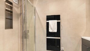 A modern bathroom with a glass shower enclosure, a black towel rack, and a white towel hanging on it. - Market Square Luxury | Modern 2-Bed City Retreat (Nottingham)