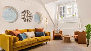 A modern living room with a yellow sofa, two armchairs, a coffee table, and decorative wall clocks. - Market Square Luxury | Modern 2-Bed City Retreat (Nottingham)