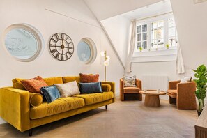 Ein modernes Wohnzimmer mit einem gelben Sofa, zwei Sesseln, einem Couchtisch und dekorativen Wanduhren.