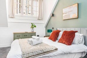A bedroom with a bed, a bedside table with a plant, a lamp, and a painting on the wall. - Market Square Luxury | Modern 2-Bed City Retreat (Nottingham)
