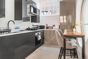 A modern kitchen with dark cabinetry, a stainless steel range hood, and a dining area with a wooden table and bar stools.