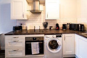 Uma cozinha compacta com armários brancos, micro-ondas, torradeira, máquina de café e máquina de lavar.