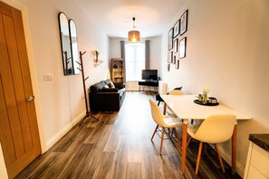 A compact living space with a dining area, a sofa, a TV, and a wooden floor. - Cosy Converted Chapel Retreat · Central Swansea (Swansea)