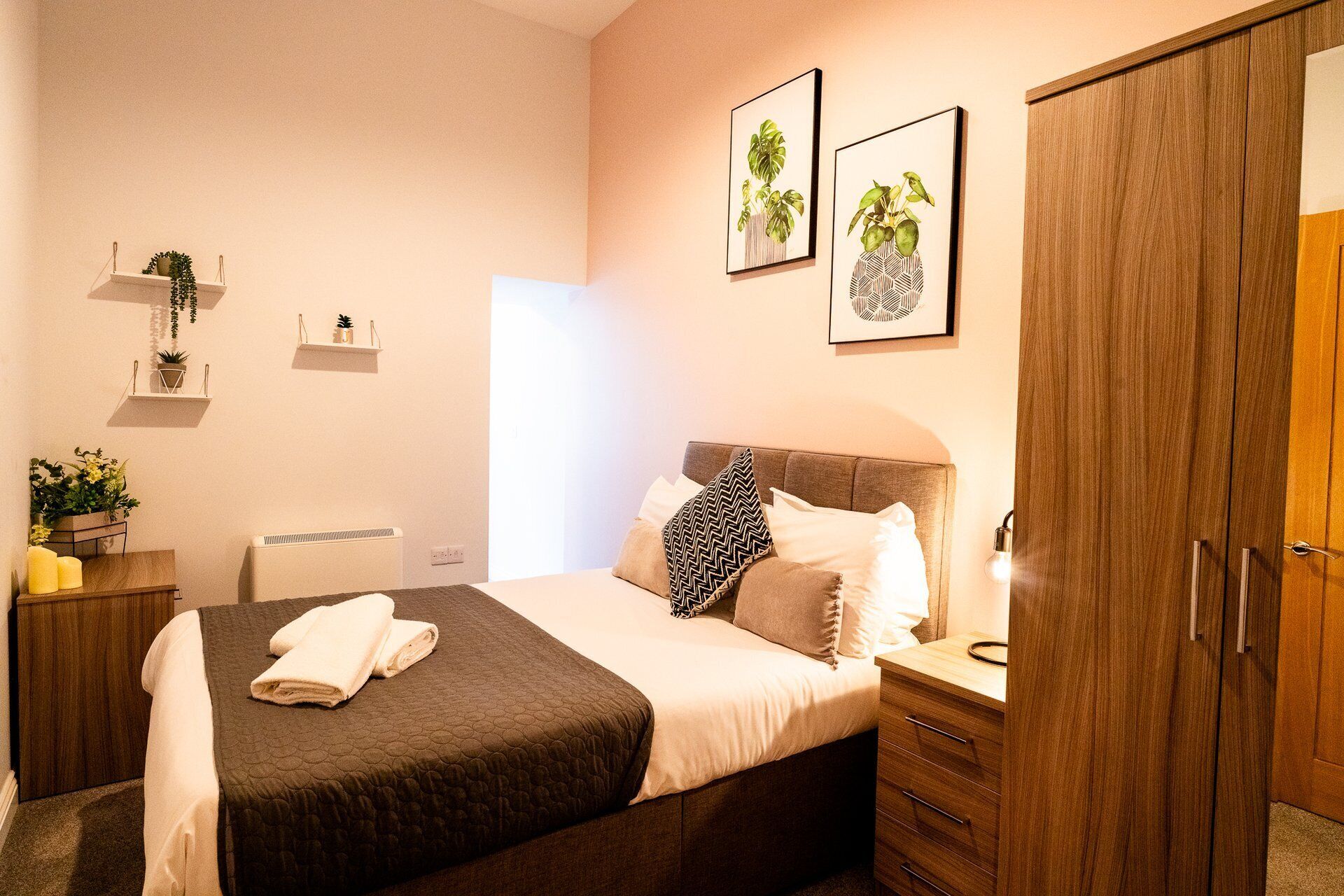 Un dormitorio ordenado con cama, mesitas de noche, armario y estanterías con plantas.