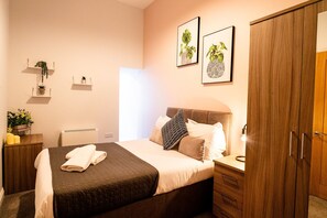Une chambre à coucher bien rangée, avec un lit, des tables de chevet, une armoire et des étagères murales ornées de plantes.