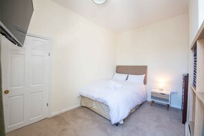 A bedroom with a bed, a nightstand, a wall-mounted shelf, and a door. - Albert Edward House – Modern 2BR Home in Liverpool (Liverpool)