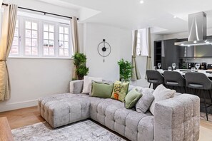 Ein modernes Wohnzimmer mit einem Ecksofa, einem Essbereich mit Barhocker und einer Küche mit Edelstahlgeräten.