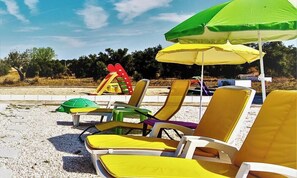 Beach chairs and umbrellas on a sandy area with a playground in the background.