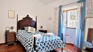 A bedroom with a wooden bed, two bedside tables, a nightstand, a window with curtains, and a wall with a framed sign.