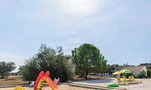 A playground with slides and swings, a large tree, and a building with a red roof.