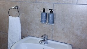 A bathroom with a white sink, a towel rack, and two hand and body wash bottles on a shelf.