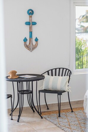 Ein Zimmer mit einem runden Tisch, einem schwarzen Metallstuhl, einem gestreiften Kissen, einem gewebten Teppich und einer Wanddekoration als Anker.
