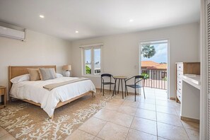 Ein Schlafzimmer mit Bett, Nachttischen, einem Teppich, einem Balkon mit Stühlen und Blick ins Freie.