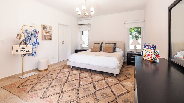Un dormitorio con cama, candelabro, alfombra estampada, mesita de noche y un perchero de pared con bolsas.
