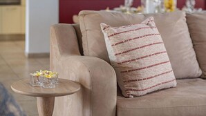 Un sofá beige con un cojín estampado y una mesita redonda con un florero de vidrio y flores.