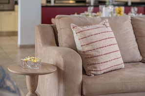 Ein beiges Sofa mit einem gemusterten Kissen und einem kleinen runden Tisch mit einer Glasvase und Blumen.