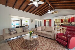 Ein Wohnzimmer mit Sofa, Sessel und Couchtisch, eine Küche mit roten Schränken und einem Deckenventilator.