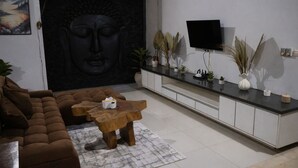 Een moderne woonkamer met een bank, een salontafel, een Boeddhabeeld, een flatscreentelevisie en sierplanten.