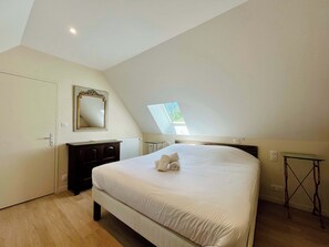 A bedroom with a bed, a dresser, a mirror, a skylight, and a small table. - Soleil Levant Exceptional Villa with Pool (Quettehou)