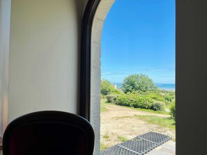 A view from inside a room with a window overlooking a grassy area and a clear blue sky. - Soleil Levant Exceptional Villa with Pool (Quettehou)