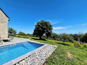 A swimming pool with a stone wall and a grassy area with a tree. - Soleil Levant Exceptional Villa with Pool (Quettehou)