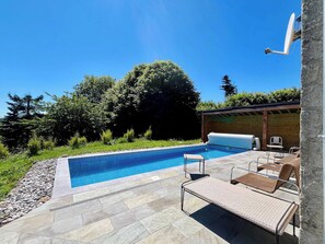 A swimming pool with lounge chairs and a covered area, surrounded by greenery. - Soleil Levant Exceptional Villa with Pool (Quettehou)