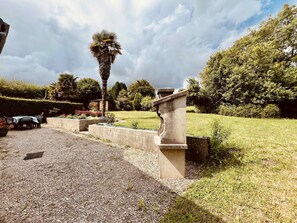 Ein Garten mit Palme, Stehbank und Kiesweg.