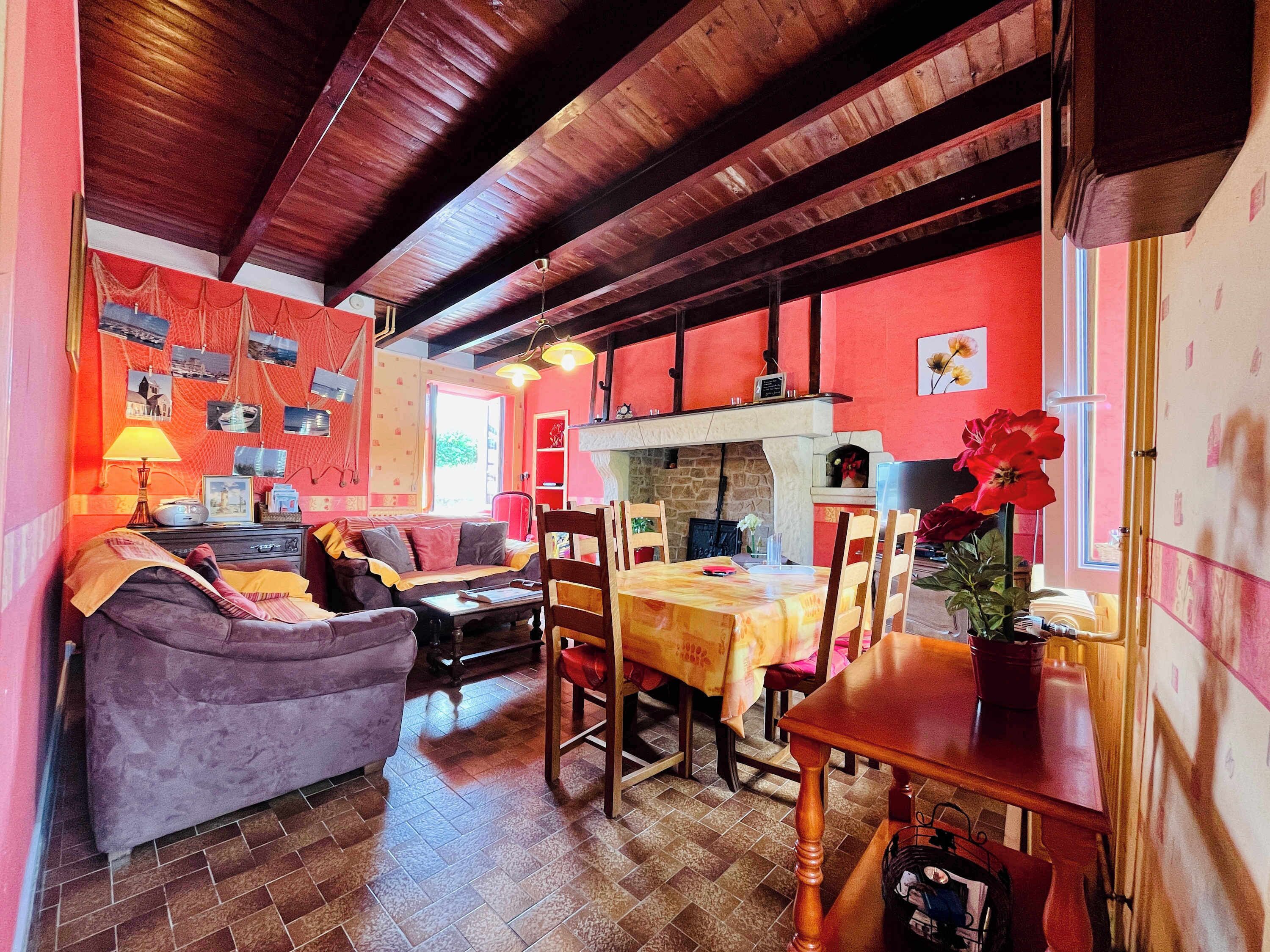 Un salon chaleureux avec un canapé, une table à manger et des chaises, une cheminée et un mur rouge orné de tableaux.
