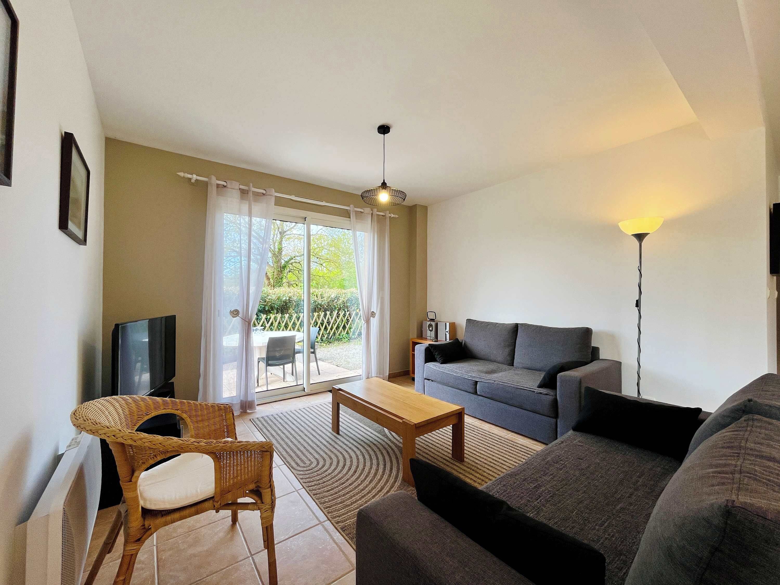 A living room with a sofa, a coffee table, a TV, and a wicker chair.