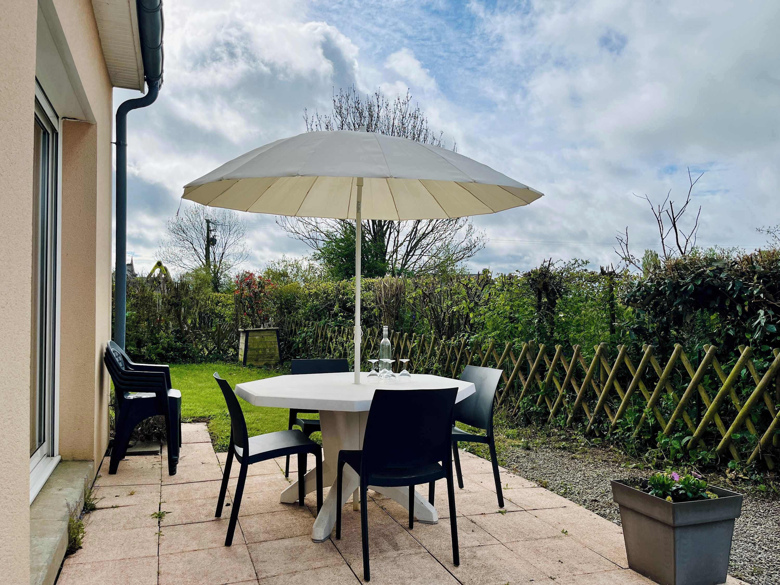 Une terrasse extérieure avec une table ronde et des chaises, un parasol et une plante en pot.