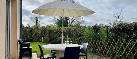 Une terrasse extérieure avec une table ronde et des chaises, un parasol et une plante en pot.