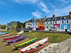 Colorful boats on a grassy area, a red van, and a row of brightly painted houses.