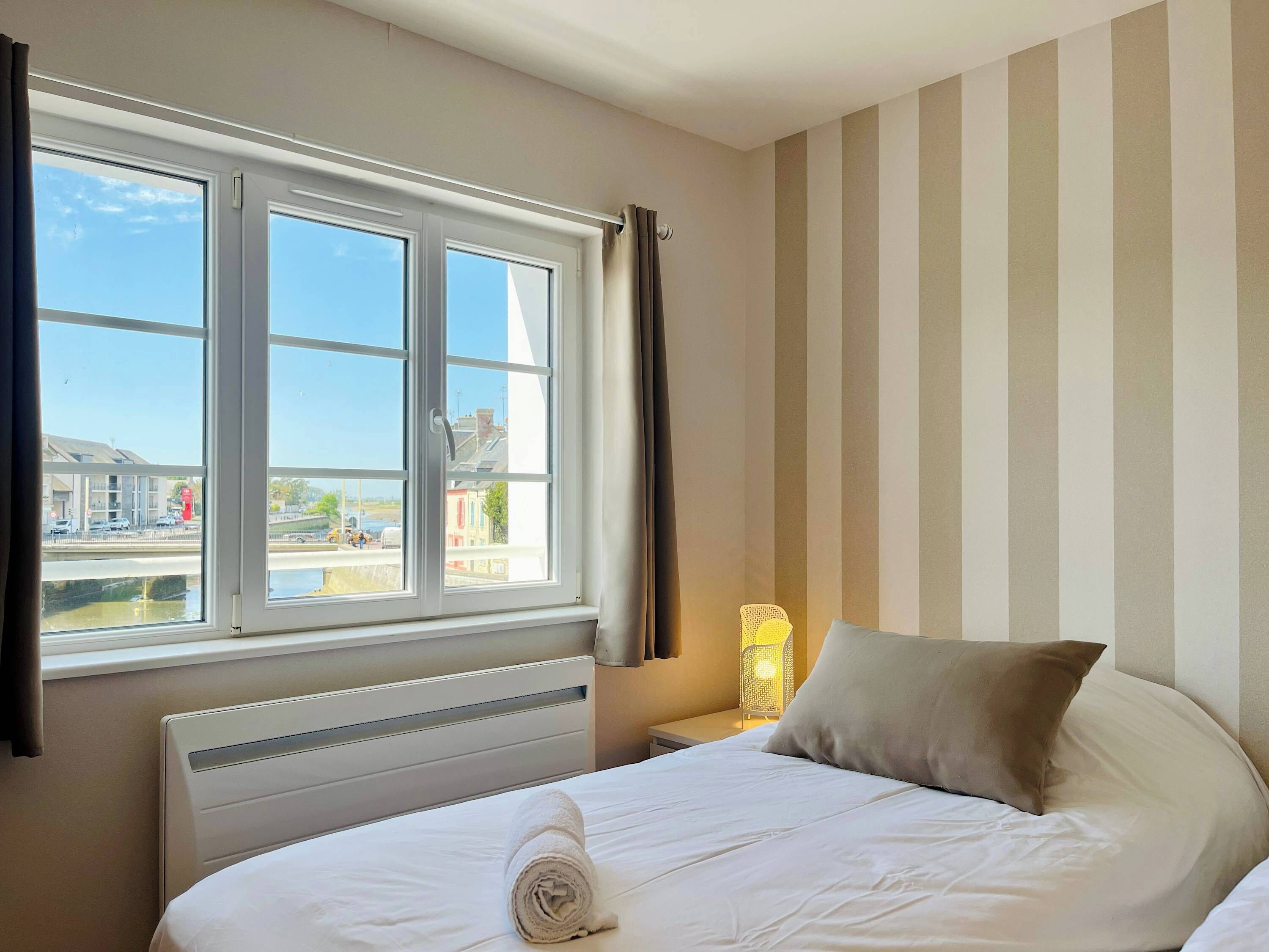 A hotel room with a bed, a window with curtains, a bedside lamp, and a view of the street outside.
