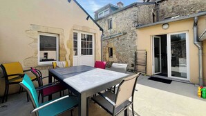 An outdoor patio with a table and chairs, a stone building, and a window. - La Maison Bleue, Authentic Fishermans House (Isigny-sur-Mer)