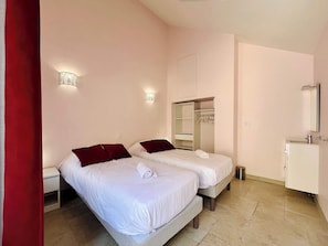 A hotel room with two beds, a wardrobe, a mirror, and a small bedside table.