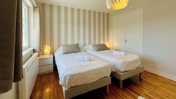 A bedroom with two beds, a striped wall, a wooden floor, a white wardrobe, and a hanging light fixture. - La Maison Bleue, Authentic Fishermans House (Isigny-sur-Mer)