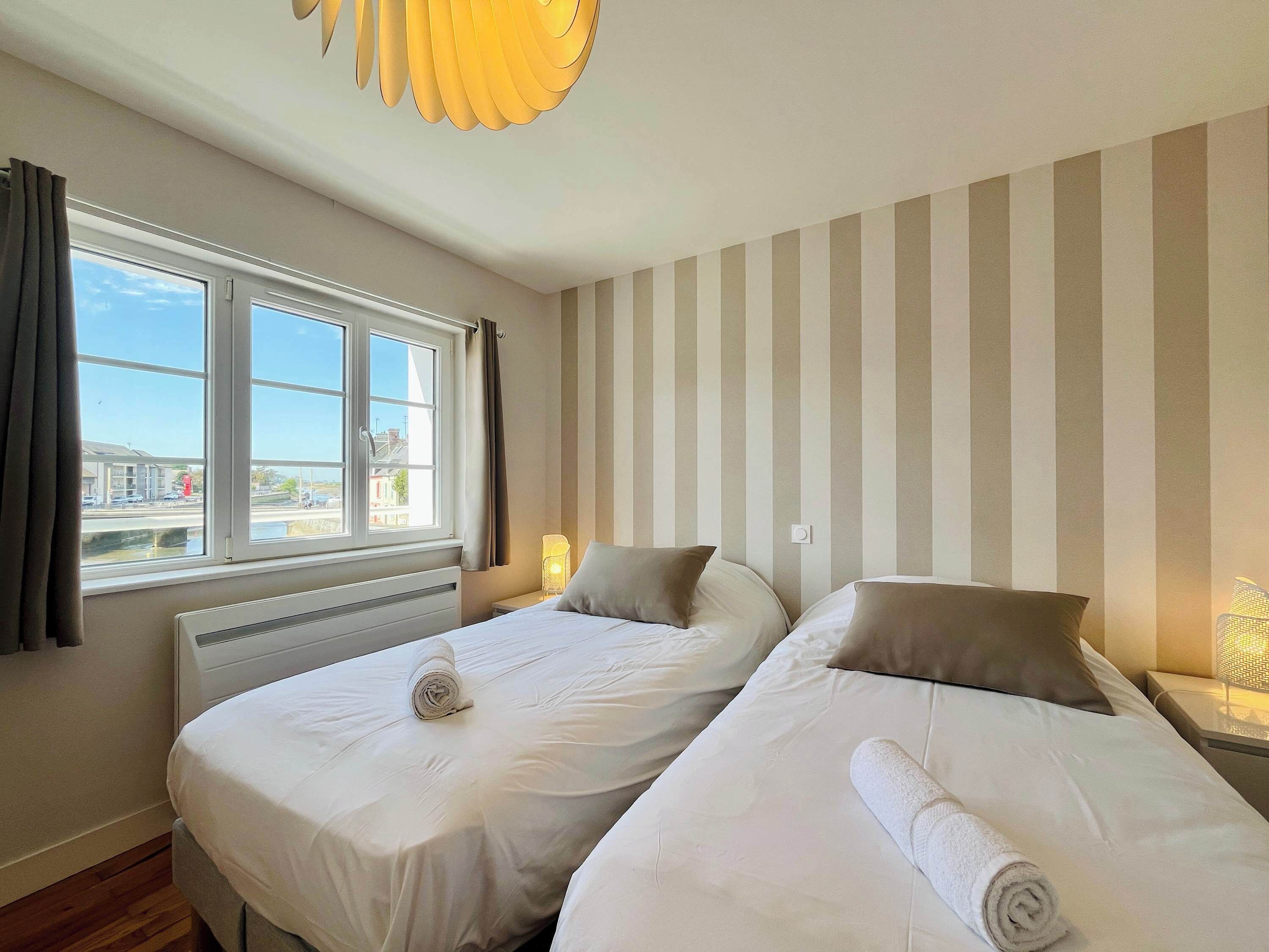 Habitación de hotel con dos camas, una ventana con cortinas, un radiador y una pared a rayas.