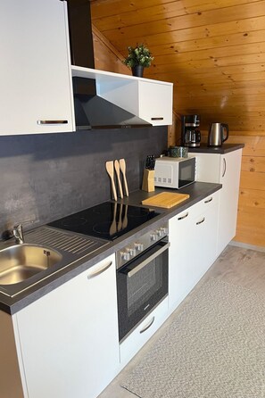 A modern kitchen with white cabinets, a black countertop, stainless steel appliances, and a wooden ceiling. - Allalinblick by Interhome (Saas-Grund)