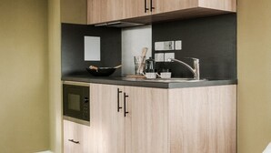 A kitchen with wooden cabinets, a microwave, and a sink. - Student Only YourTRIBE EC (London)