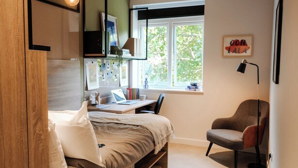 A bedroom with a bed, desk, chair, window, and a wall-mounted shelf. - Student Only YourTRIBE EC (London)