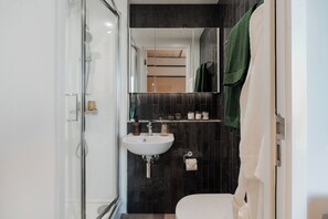 Ein modernes Badezimmer mit Duschkabine aus Glas, einem weißen Waschbecken und einer dunkel gefliesten Wand.