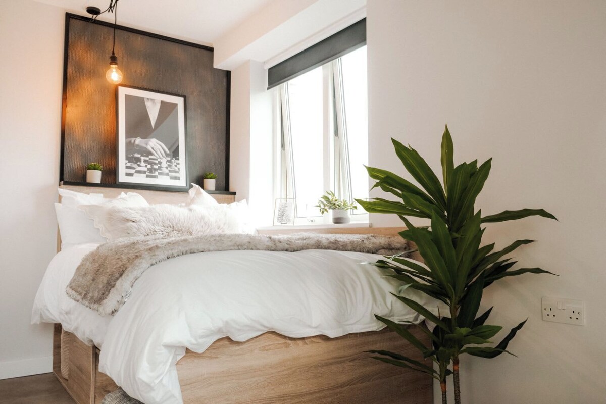 Ein Schlafzimmer mit Bett, einer Pendelleuchte, einem Fenster und einem Blumentopf.